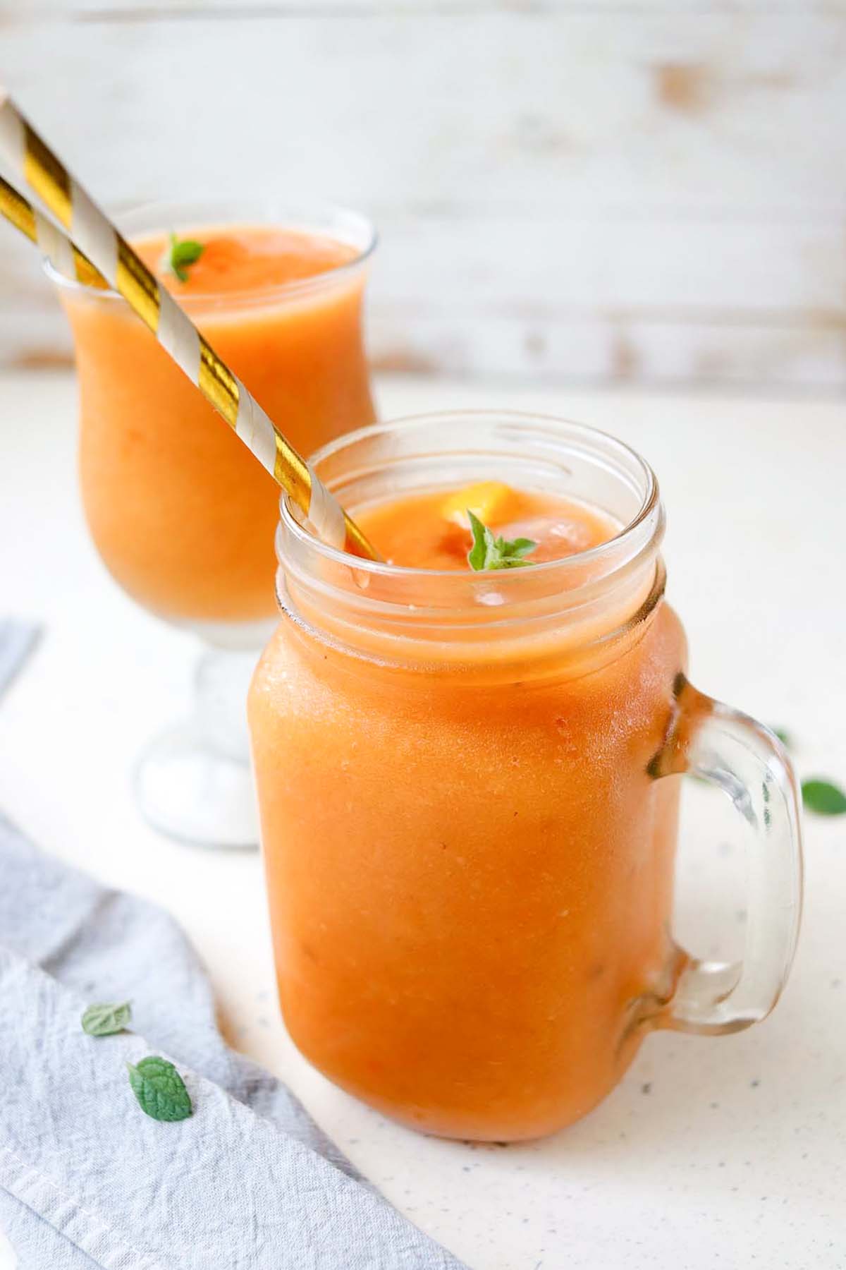 two orange smoothies in glasses with straws.